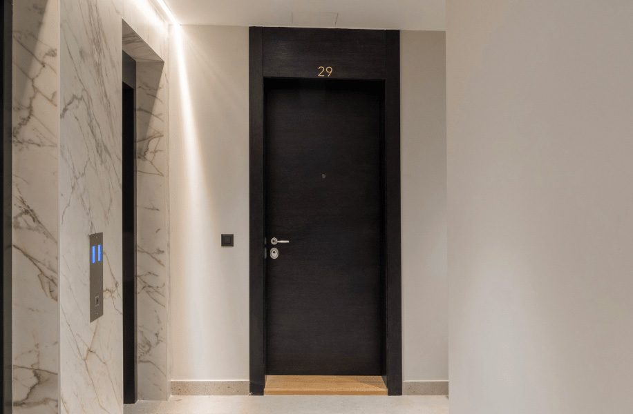 Modern black entrance door in an elegant residential hallway with marble walls and elevators