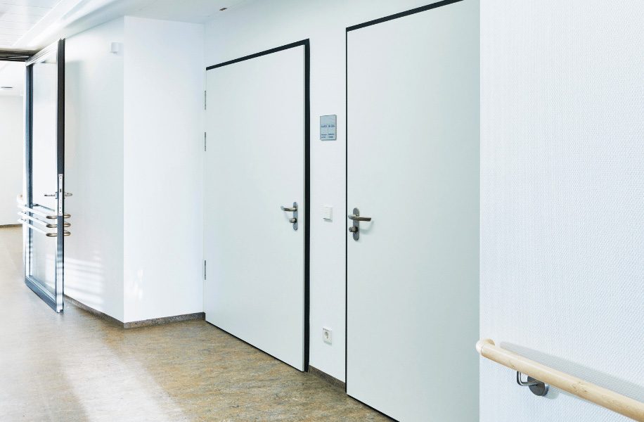 Portes intérieures blanches avec poignées en acier inoxydable dans un couloir institutionnel moderne