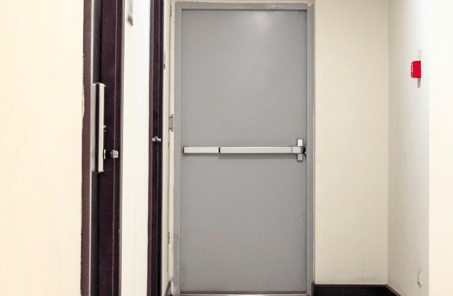 Porte coupe-feu grise avec barre anti-panique dans un corridor d’immeuble