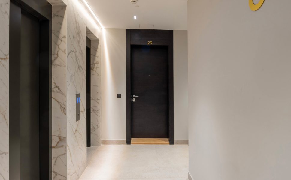 Modern apartment entrance door in hallway with elevators and marble walls